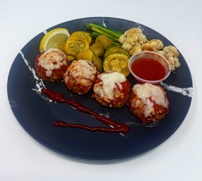 Plated dish with meatballs, vegetables, and a side of sauce on a white background