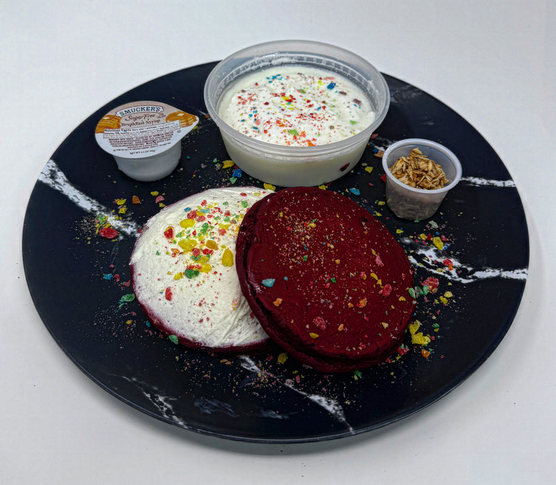 Two colorful pancakes on a black marble plate with side dishes.
