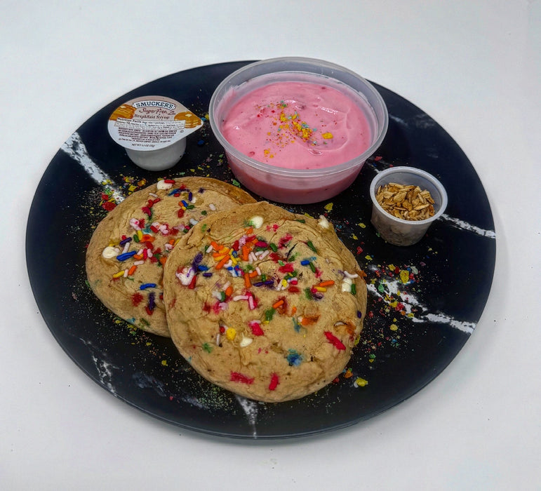 Cookies with colorful sprinkles on a black plate with pink icing and nuts.
