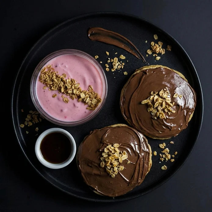 Two chocolate-glazed donuts with a side of pink yogurt and granola on a black plate.