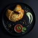 Two empanadas on a black plate with a side of salsa and guacamole.