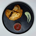 Two empanadas on a black plate with a side of salsa and guacamole.