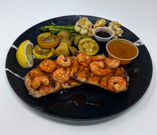 Plated dish with shrimp, salmon, vegetables, and sauces on a black plate.