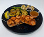 Plated dish with shrimp, salmon, vegetables, and sauces on a black plate.