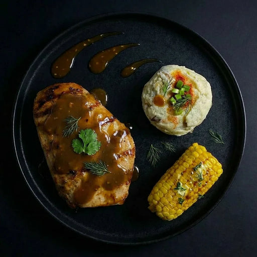 Plated dish with meat, corn, and a side dish on a dark background