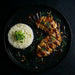 Plated dish with sliced meat, rice, and herbs on a dark background. Meal made by the halal meal prep.