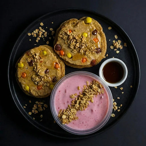 Two pancakes with toppings on a black plate with a side of yogurt and syrup.