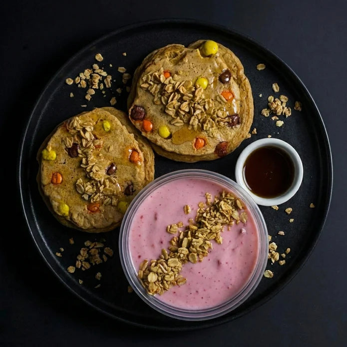 Two pancakes with toppings on a black plate with a side of yogurt and syrup.