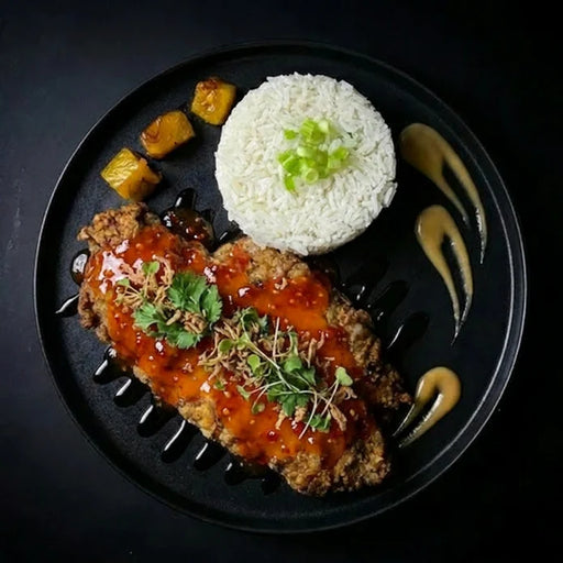 Plated dish with breaded meat, white rice, and pineapple chunks on a black plate.