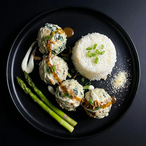 Plated dish with meatballs, rice, and asparagus on a black plate. The Halal Meal Prep
