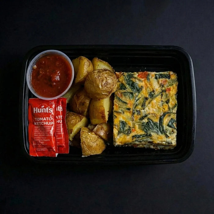 Meal in a black tray with frittata, potatoes, and Hunt's tomato ketchup on a dark background