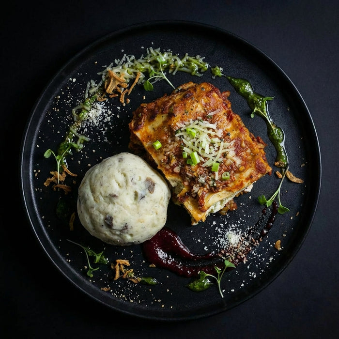 Plated dish with lasagna, garlic bread, and a side of mashed potatoes on a dark background. Meal made by the halal meal prep.