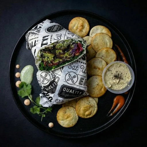 Burrito on a black plate with chips and condiments on a dark background