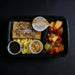 Breakfast meal in a black tray with French toast, fruit, and scrambled eggs on a dark background.