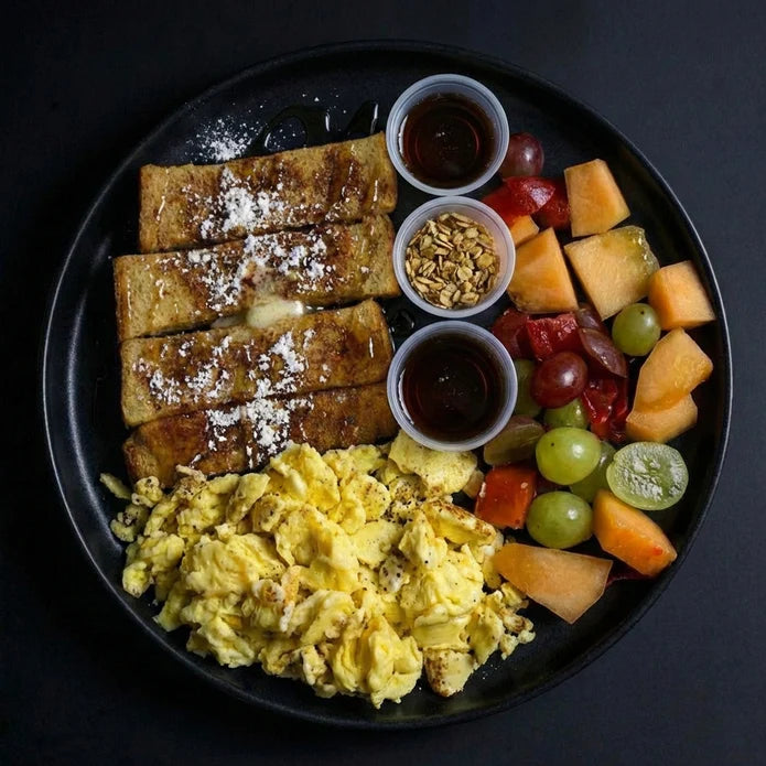 Breakfast plate with French toast, scrambled eggs, and fruit on a black plate.