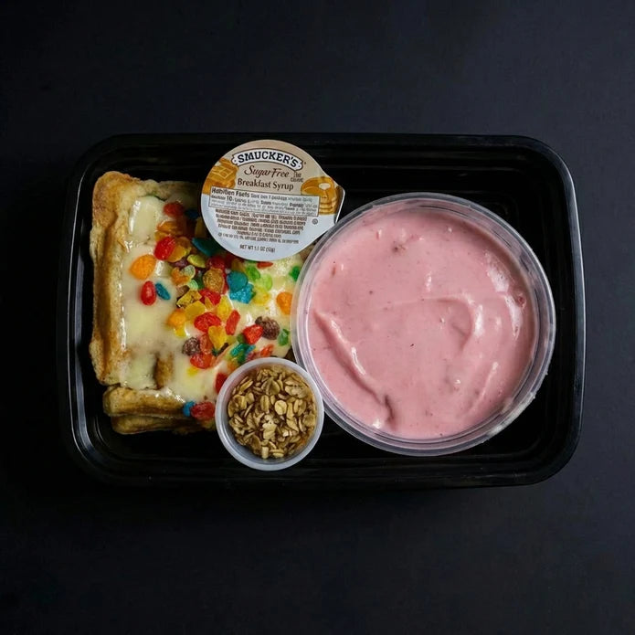 Prepared meal with dessert item, yogurt, and granola in a black tray on a dark background