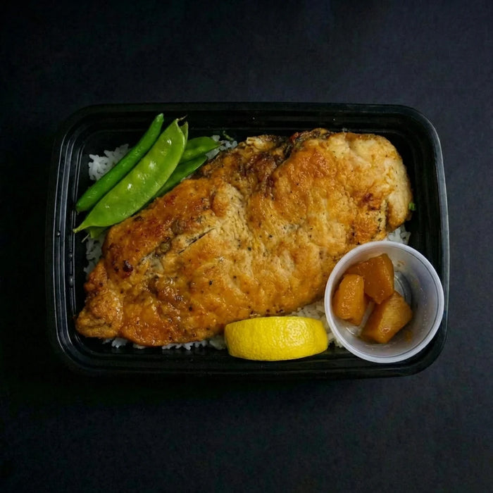 Plated meal with fried fish, green beans, lemon, and a side dish on a dark background