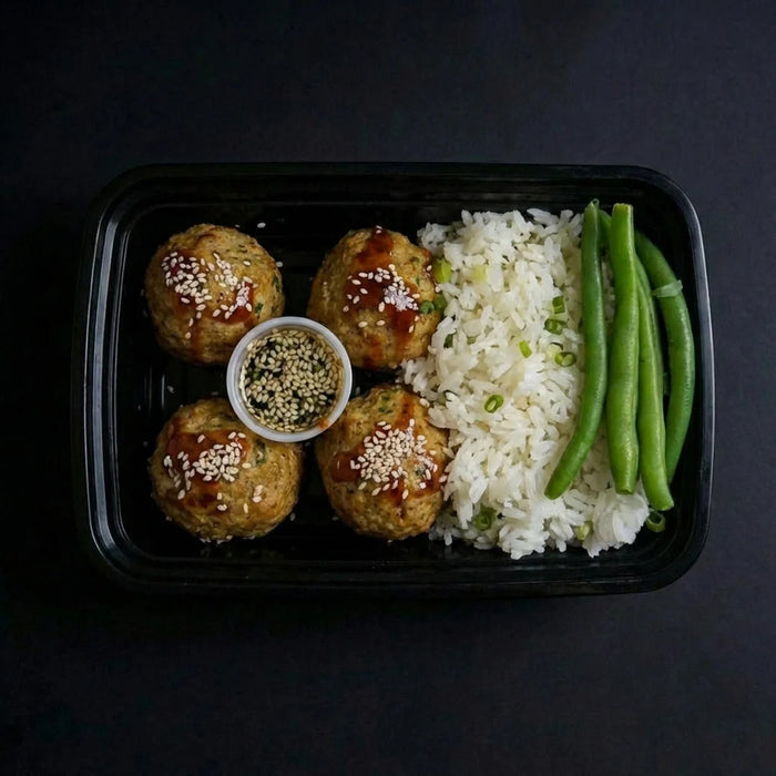Plated meal with meatballs, rice, and green beans on a dark background