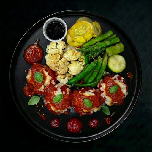 Plated dish with meatballs, vegetables, and a side of sauce on a dark background