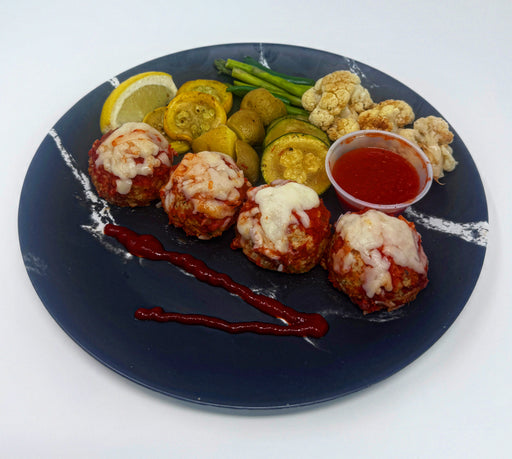 Plated dish with meatballs, vegetables, and a side of sauce on a white background