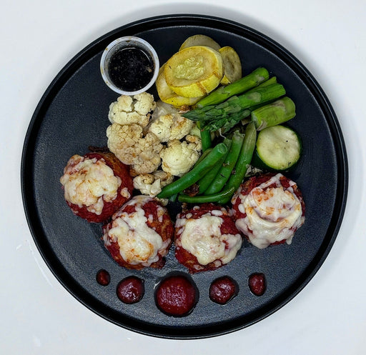 Plated dish with meatballs, vegetables, and a side of sauce on a black plate.