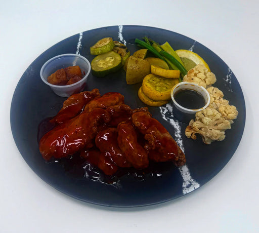 Plated dish with wings, vegetables, and sauces on a dark plate.