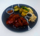 Plated dish with wings, vegetables, and sauces on a dark plate.