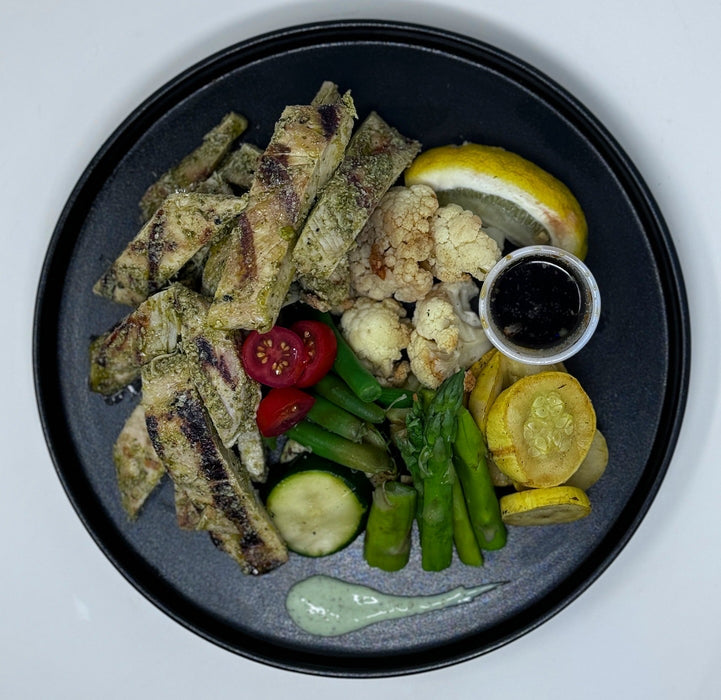 Plated dish with grilled vegetables, including zucchini, tomatoes, and asparagus, on a black plate.