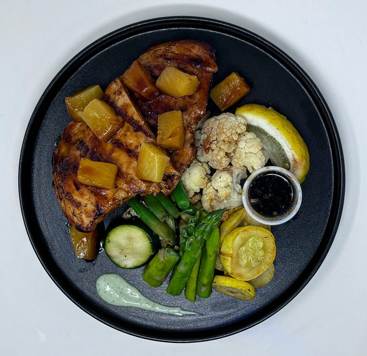 Plated dish with grilled meat, vegetables, and sauces on a black plate. a meal made by the halal meal preps.