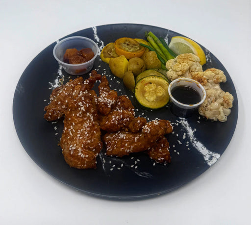 Plated dish with fried chicken, vegetables, and sauces on a black plate.