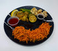 Assorted vegetables on a black plate with dipping sauces on a white background