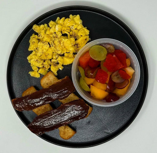 Breakfast plate with scrambled eggs, toast with chocolate spread, and fruit on a black marble-patterned plate.