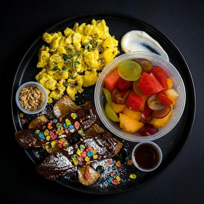 Breakfast platter with scrambled eggs, waffles, and fruit salad on a black plate.