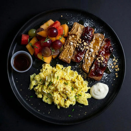 Plated meal with scrambled eggs, fruit salad, and roasted meats on a dark surface