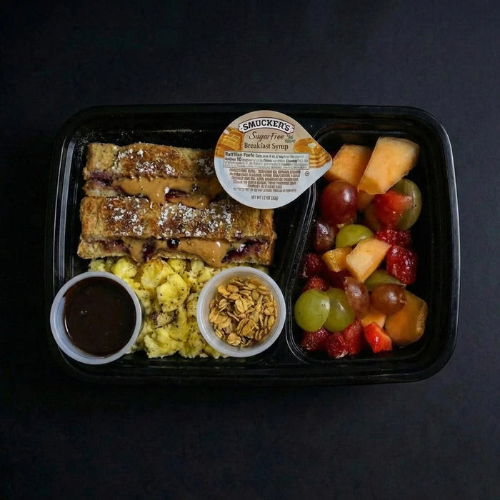 Breakfast meal in a black tray with French toast, fruit, and syrup on a dark background
