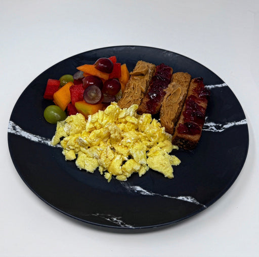 Breakfast plate with scrambled eggs, fruit, and meat on a black marble plate.