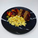 Breakfast plate with scrambled eggs, fruit, and meat on a black marble plate.