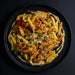 Pasta dish with chicken and vegetables on a black plate