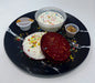 Two colorful pancakes on a black marble plate with side dishes.