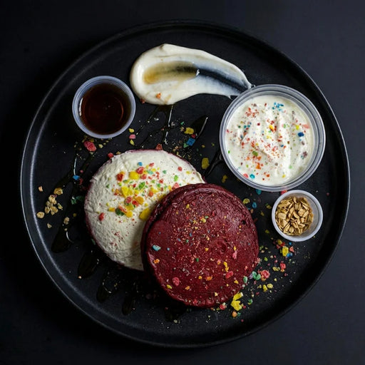Three colorful pancakes on a black plate with various toppings and sauces.