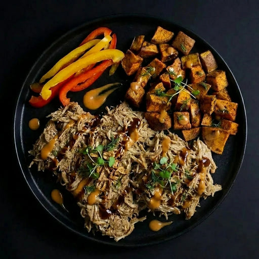 Plated dish with pulled meat, roasted sweet potatoes, and bell peppers on a dark background. The Halal Meal Preps