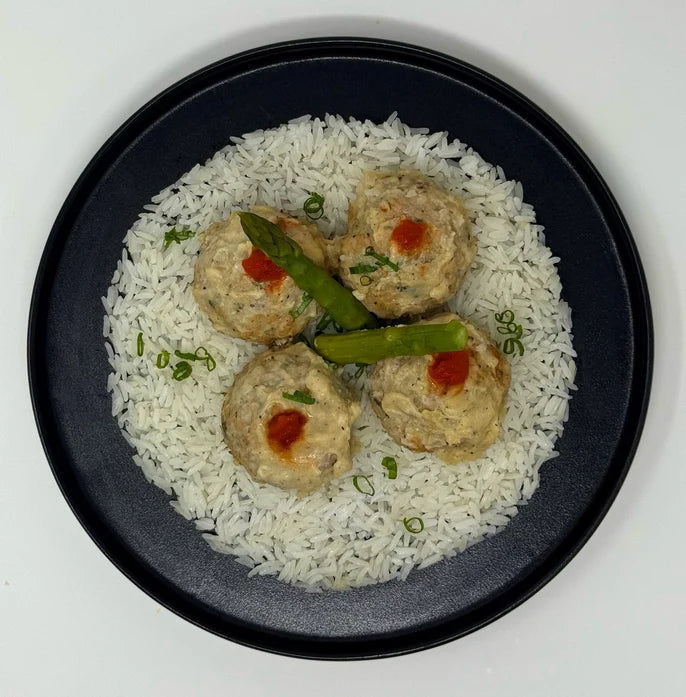 Dish with rice, meatballs, and asparagus on a white background