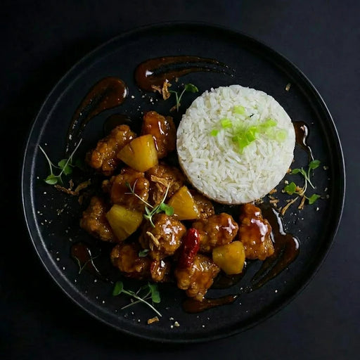 Plated dish of sweet and sour chicken with a side of rice on a dark background