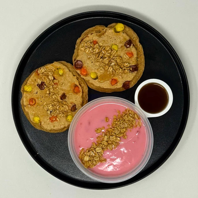 The Halal Meal Prep - Reeses PB Protein Pancakes -2 pancakes paired with a strawberry yogurt and granola on a black plate. 
