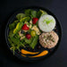 Plated food arranged to resemble a face with salad, rice, and meat patty on a dark background