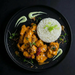 Plated dish with orange chicken and white rice on a dark background. The Halal Meal Prep