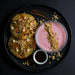 Two cookies with sprinkles and a pink yogurt bowl with granola on a black plate.