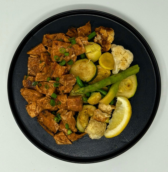 Black plate with fried tofu and vegetables on a white background