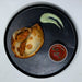 Empanada with a side of salsa and green sauce on a dark plate